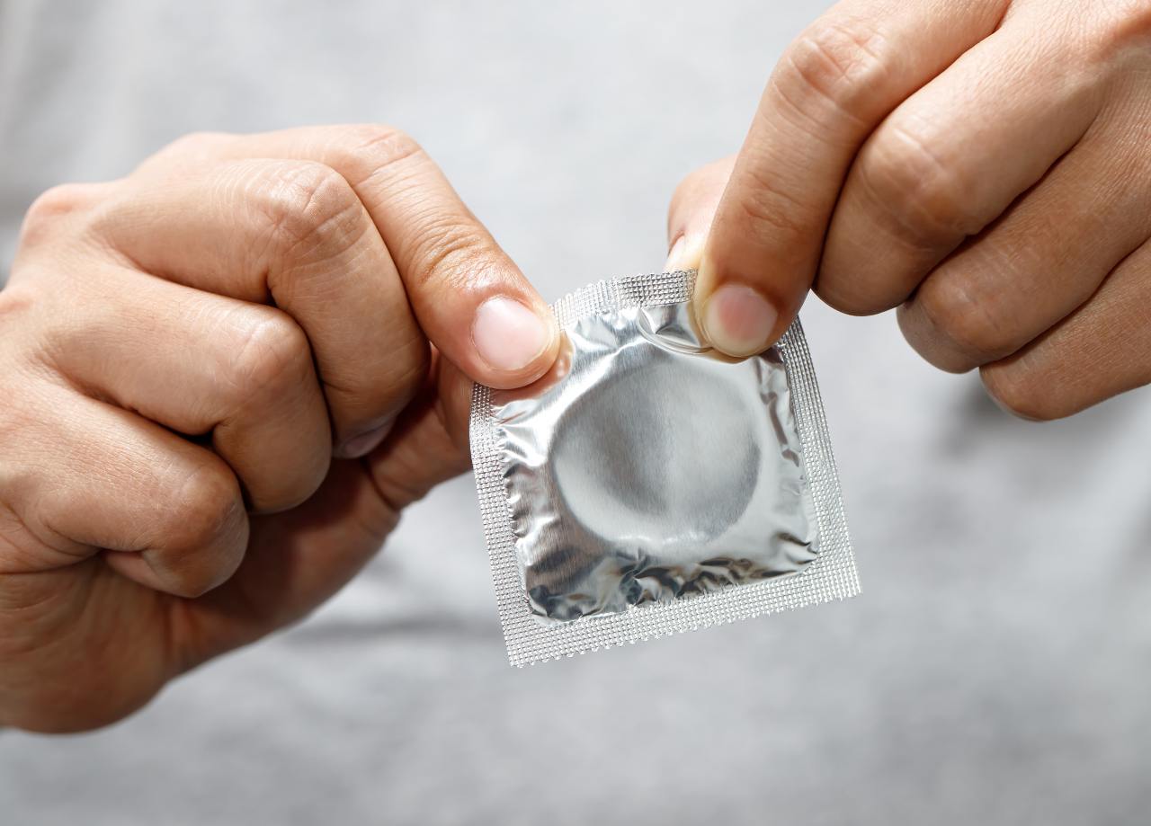 Mann mit weißem T-Shirt öffnet Kondom